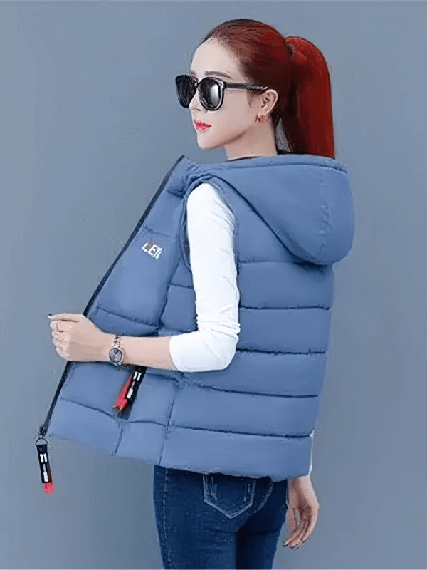 Woman wearing a blue hooded down vest with zipper pockets, stylish and functional for cooler temperatures, paired with jeans.