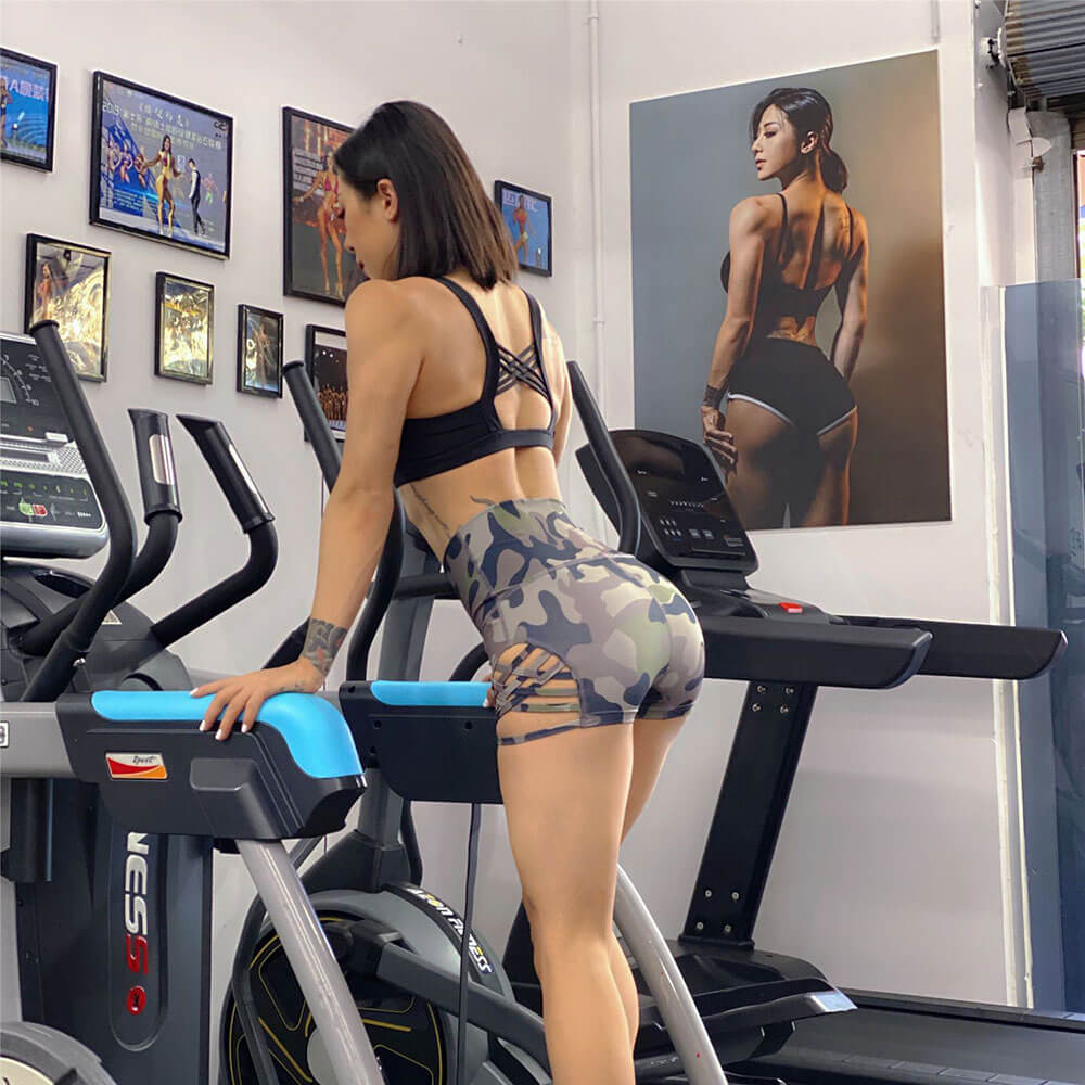 Woman wearing high waist camo shorts with side cross design exercising on a treadmill in a gym setting.