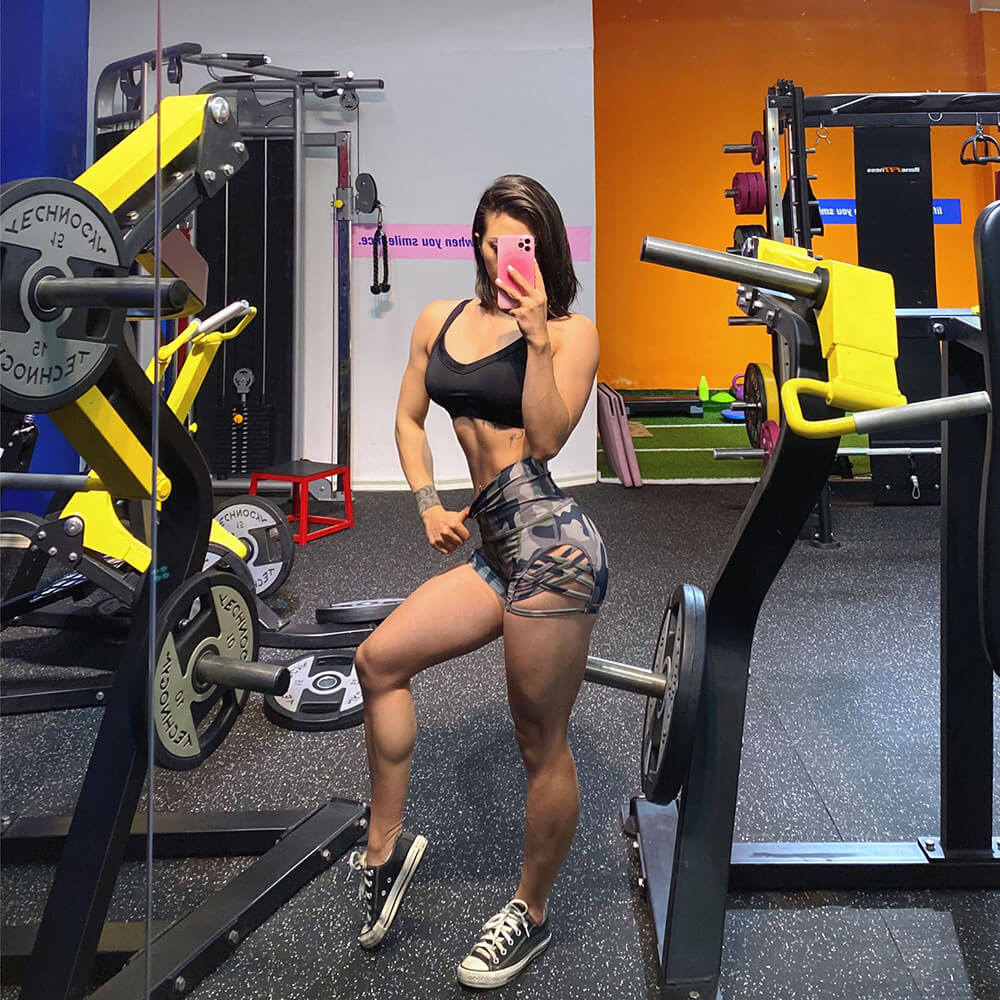 Woman wearing high waist side cross hollow shorts, lifting weights in gym. Stylish and breathable nylon-spandex fitness wear.