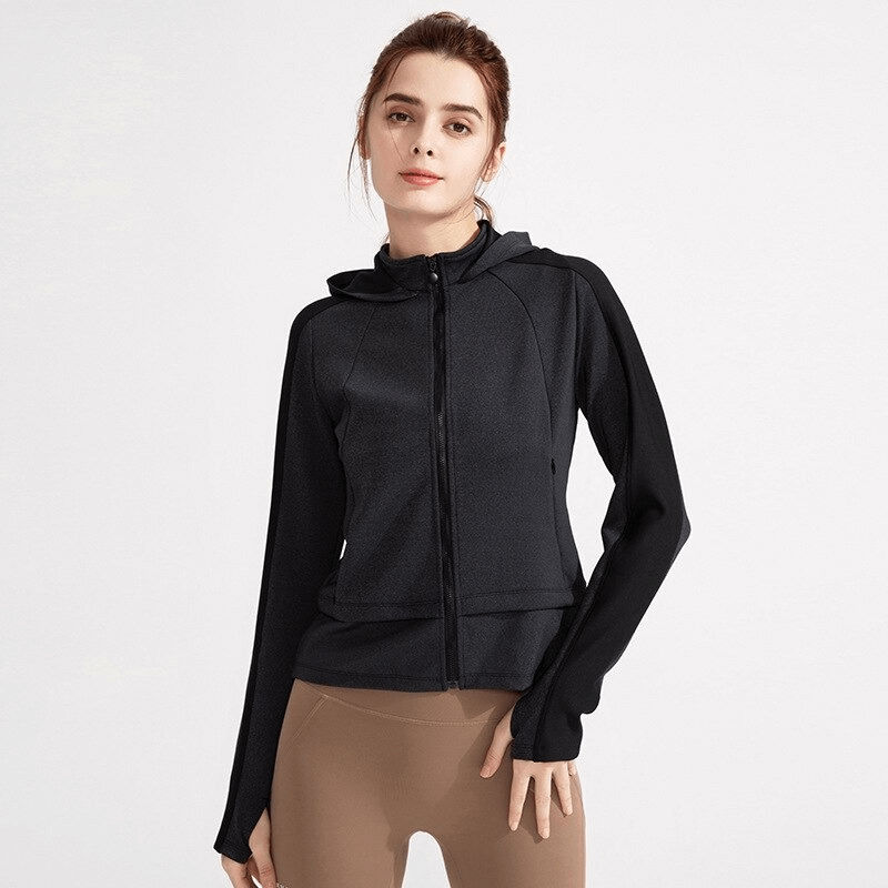 Woman modeling black hooded sweatshirt with zipper and thumb hole sleeves, ideal for workouts; made of breathable nylon and spandex.