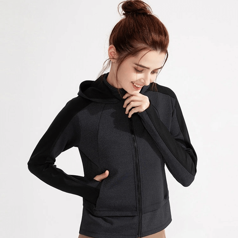 Woman wearing black hooded sweatshirt with zipper and thumb holes, ideal for sports. Comfortable, breathable, and stylish workout wear.
