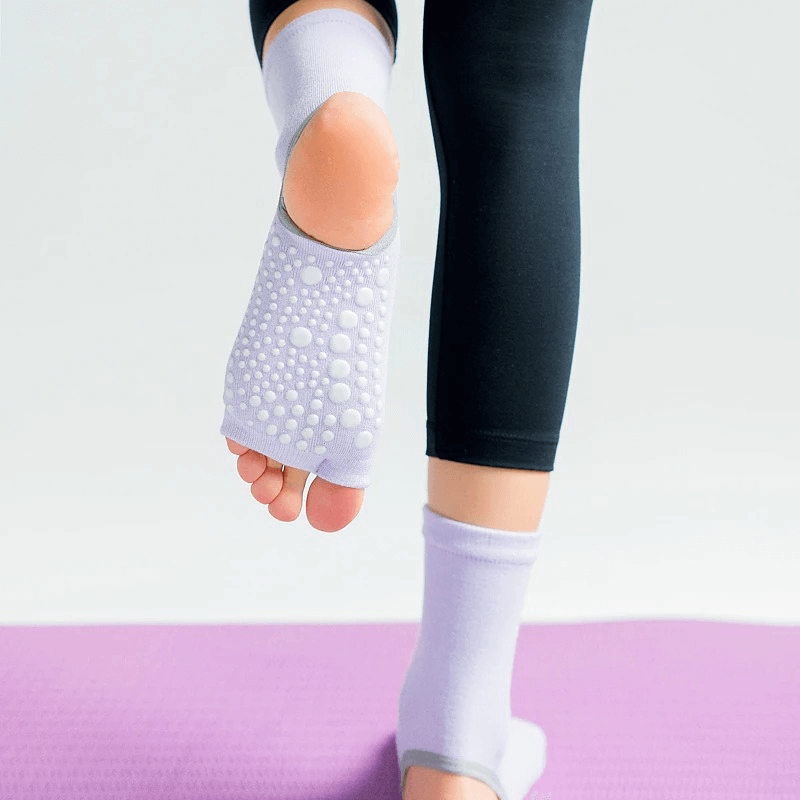Woman wearing open toe non-slip yoga socks with silicone sole on purple mat, showcasing grip and comfort for fitness activities.