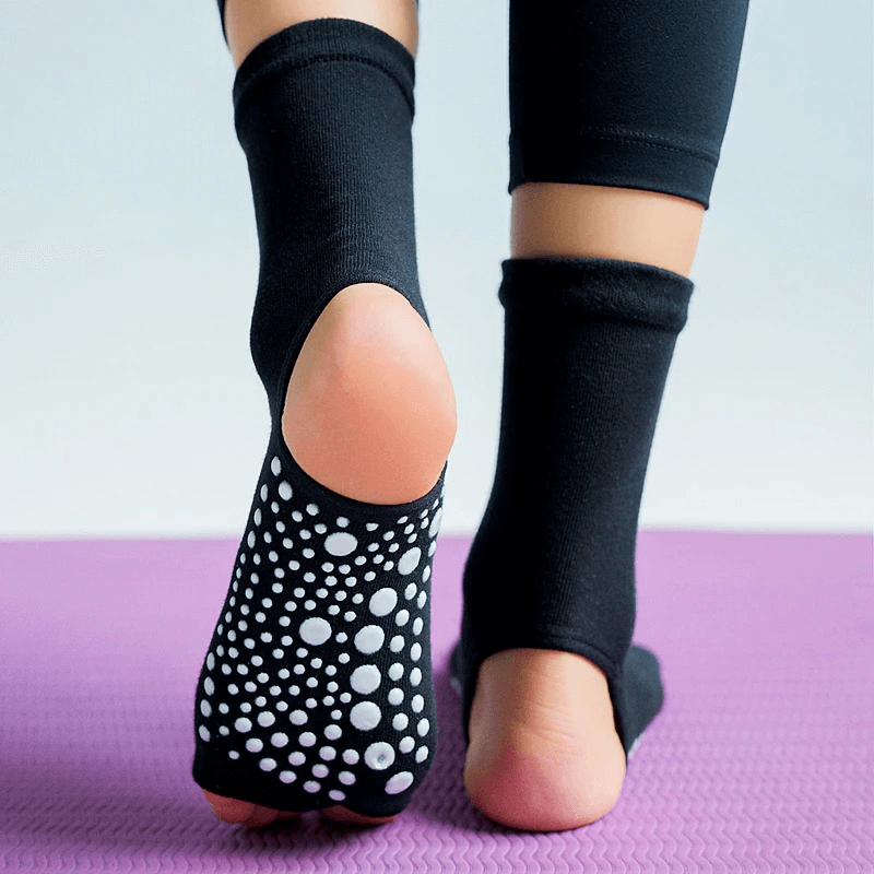 Woman wearing black open toe non-slip yoga socks with silicone sole on a purple mat, showing enhanced grip and flexibility.