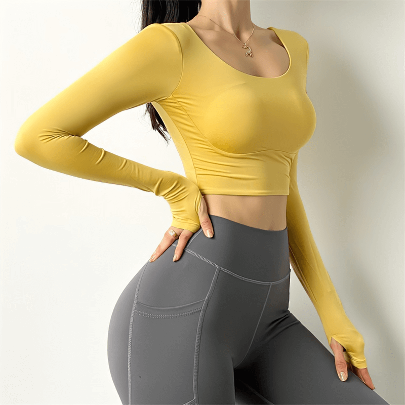 Woman wearing a yellow sexy back long sleeves sports top, designed for yoga and gym workouts, paired with gray leggings.