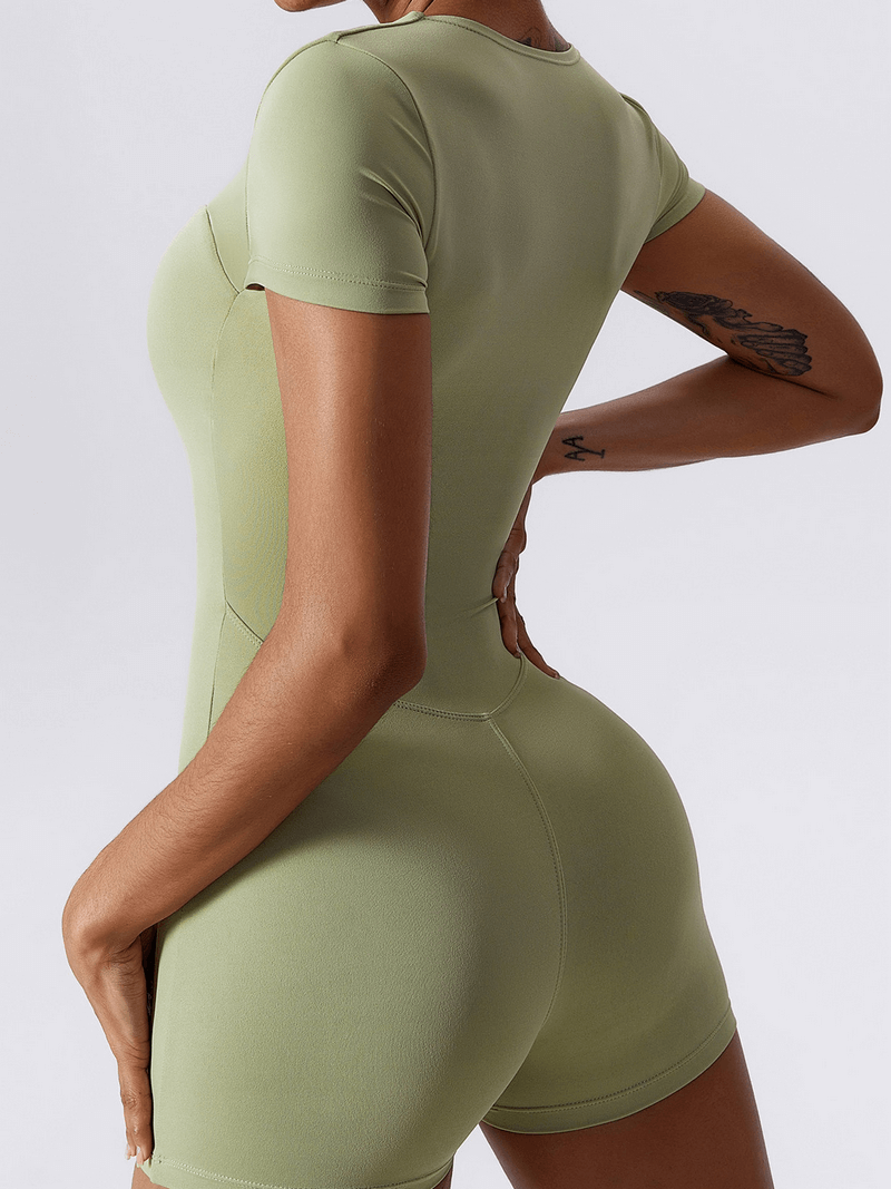 Back view of woman wearing a green short one-piece sports suit, showcasing a flattering fit ideal for fitness training.