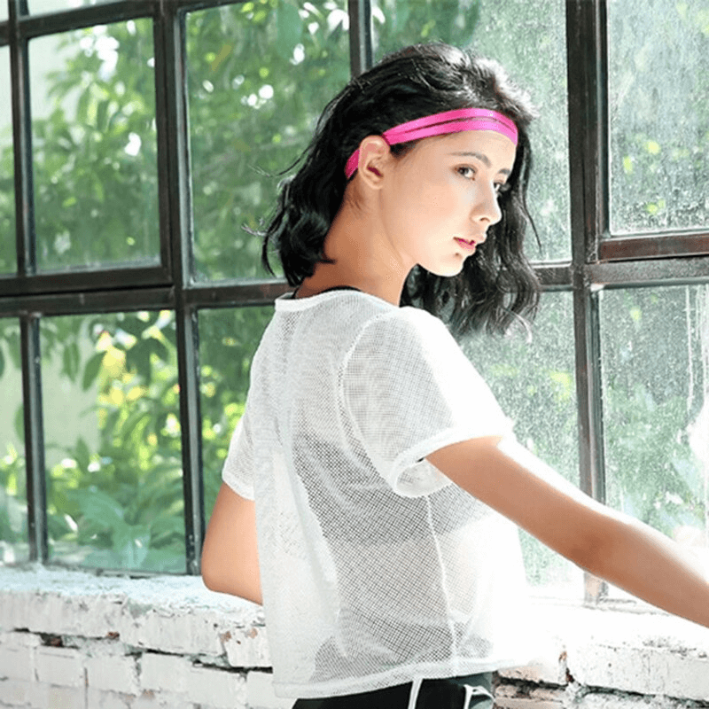 Woman wearing white mesh t-shirt, ideal for fitness and casual wear, stands by window with green plants visible outside.