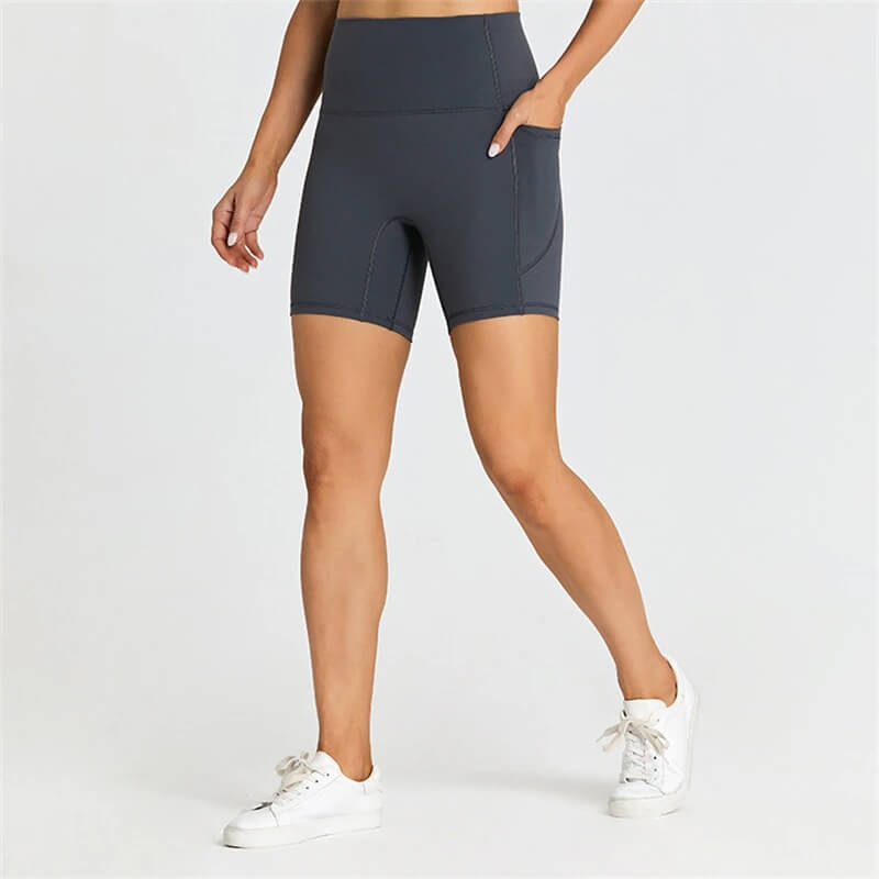 Woman wearing gray short tight solid-colored shorts with pockets, ideal for workouts, made from nylon and spandex for comfort and flexibility.