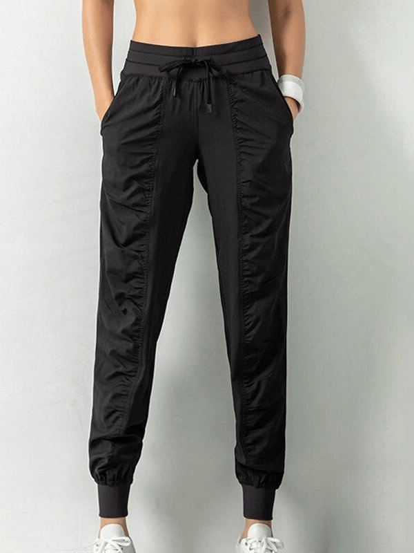 Women's black sports joggers with side pockets, cuffed hems, drawstring waist, and pleated front, perfect for casual and stylish comfort.