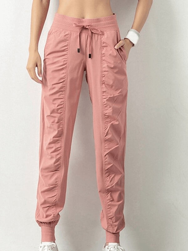 Women's pink sports joggers with side pockets, cuffs, and drawstring waist, featuring a pleated front and loose fit.