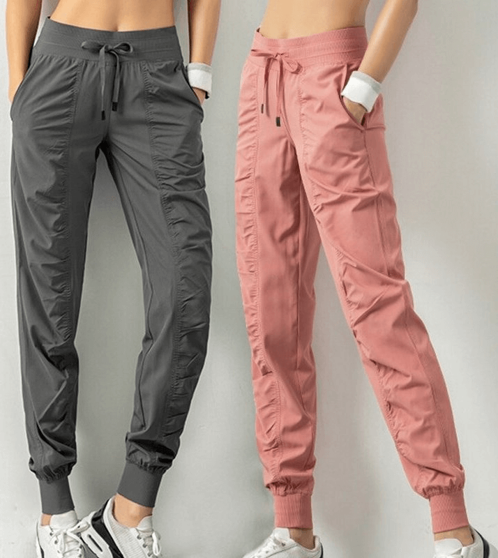 Two pairs of women's sports joggers with side pockets and cuffs, one in pink and one in gray, showcasing comfort and style with drawstring waists.