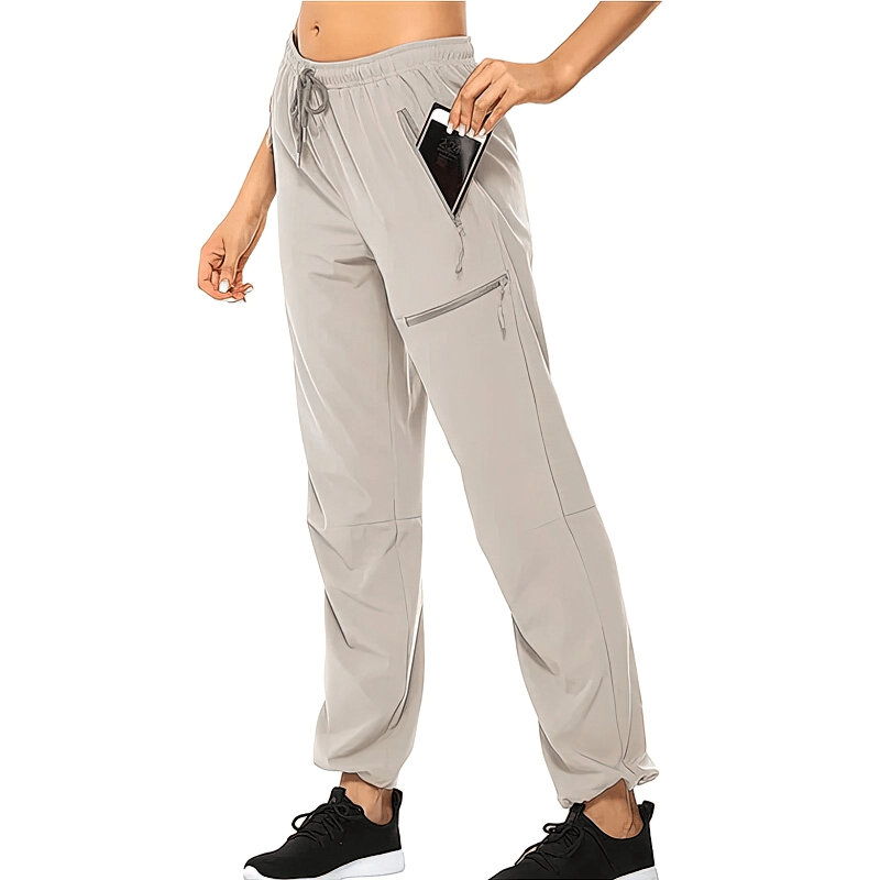 Woman in waterproof quick-drying hiking pants, featuring pockets, beige color, with phone tucked in pocket, showcasing sporty style.