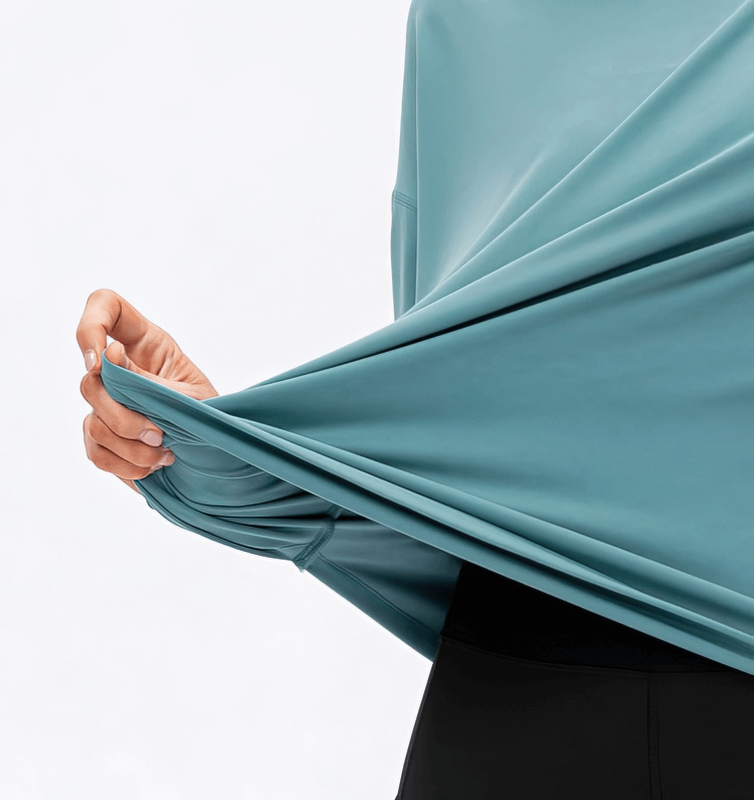 Woman holding stretchy blue loose top with long sleeves showing flexibility for sporty activities.