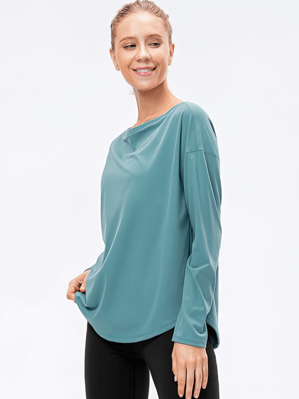 Woman wearing teal sporty light loose top with long sleeves and a loose neckline, modeled in a stylish pose.