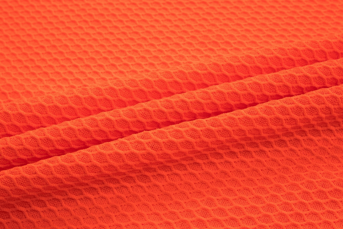 Close-up of orange textured fabric used in women's ultralight cycling base layer top, showcasing detailed weave pattern.