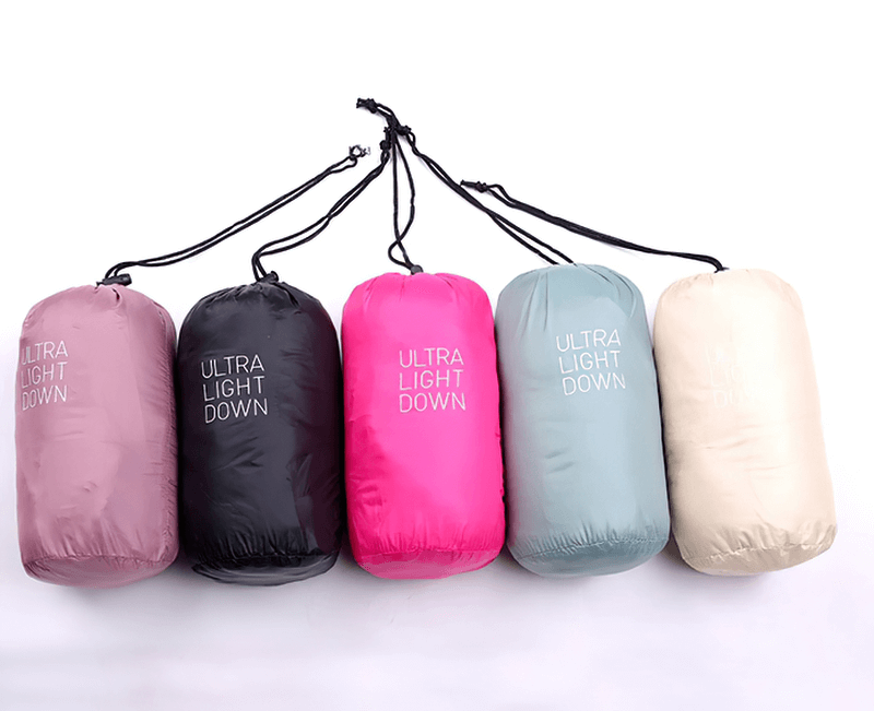Five colorful ultra-light down vests in compact carry bags lined up.